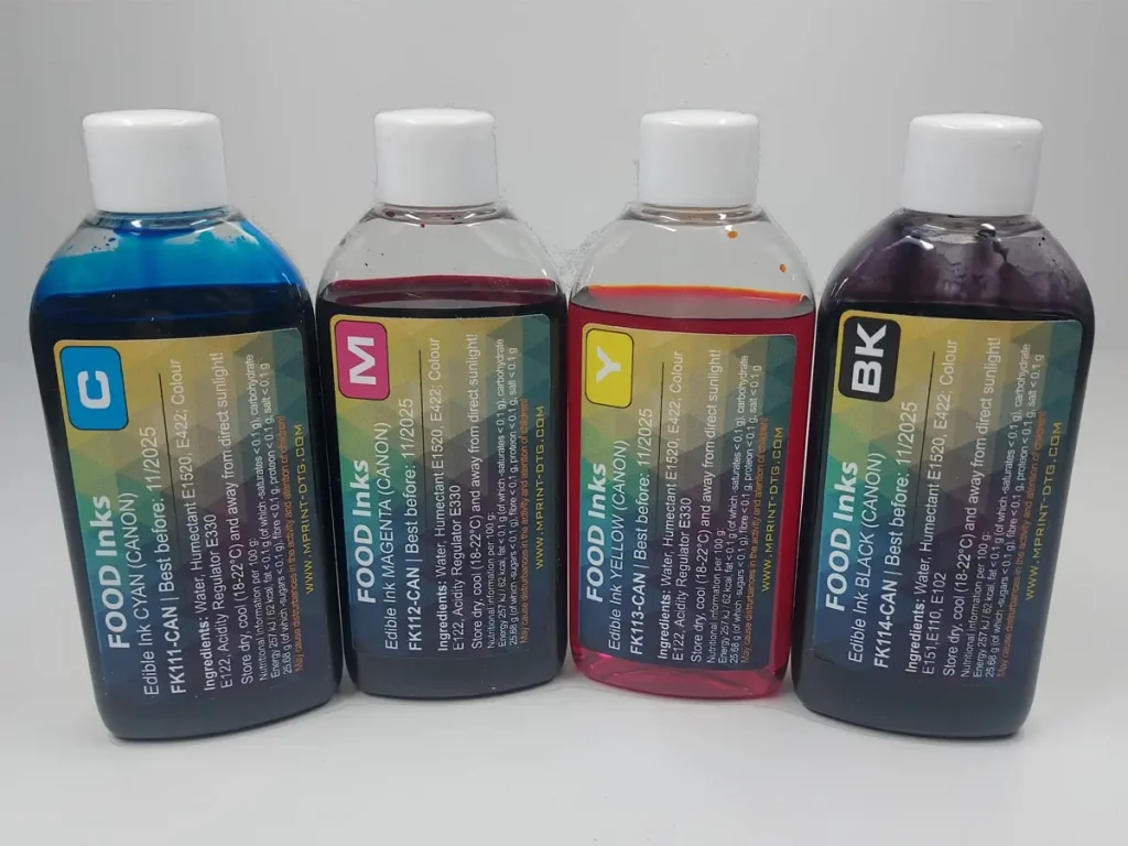 Four ink bottles with white caps in cyan, magenta, yellow, and black, arranged in a row on a light gray surface.